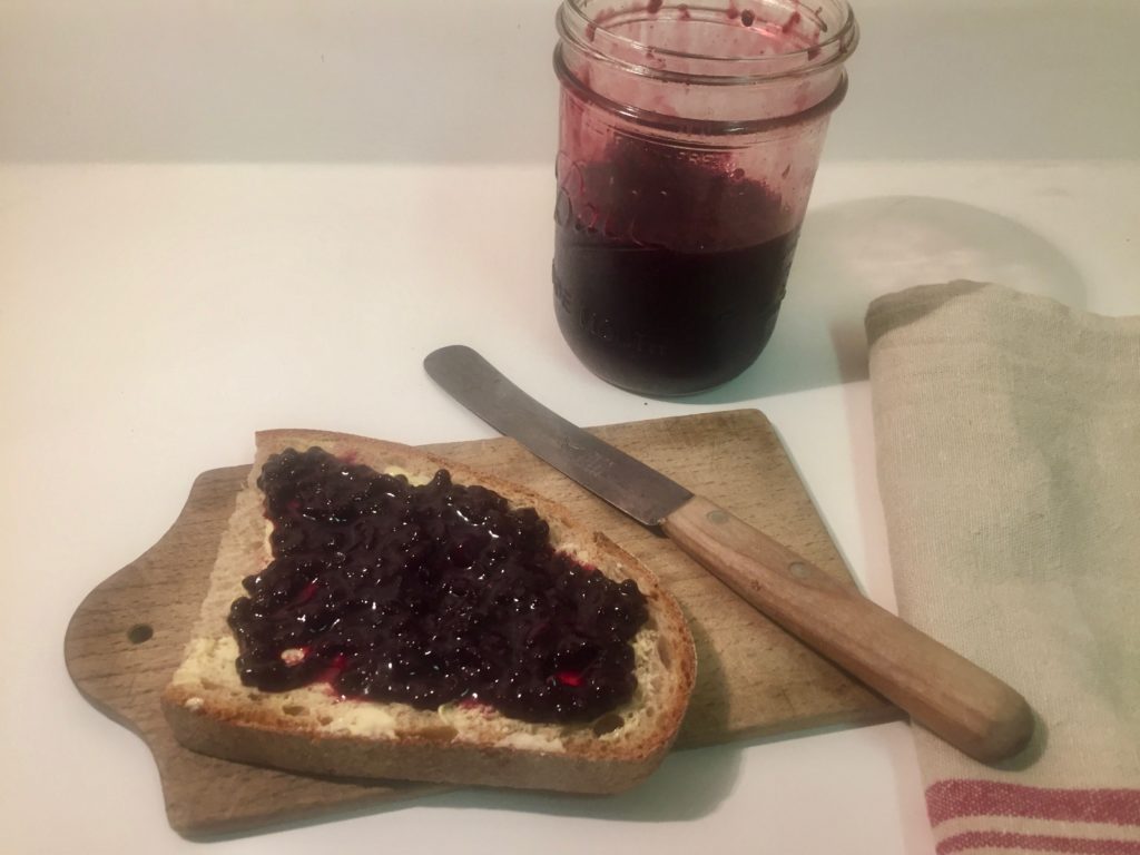 a piece of toast with butter and elderberry jam with jar of jam on kitchen counter