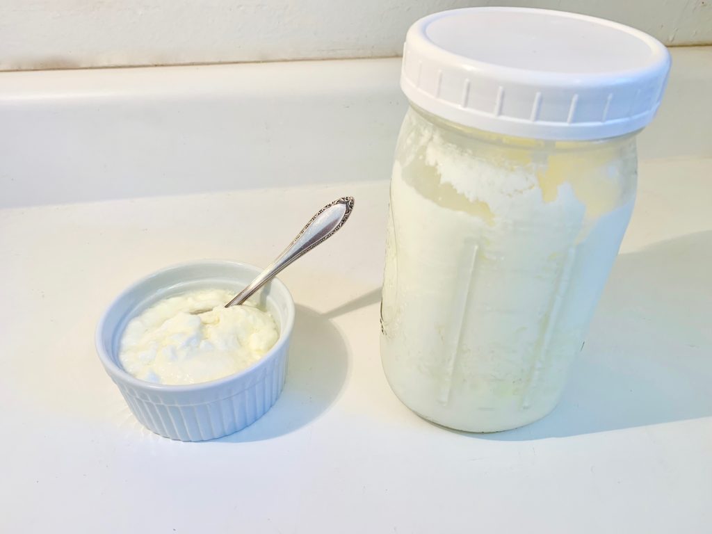 homemade yoghurt in small bowl next to a quart size mason jar with yogurt