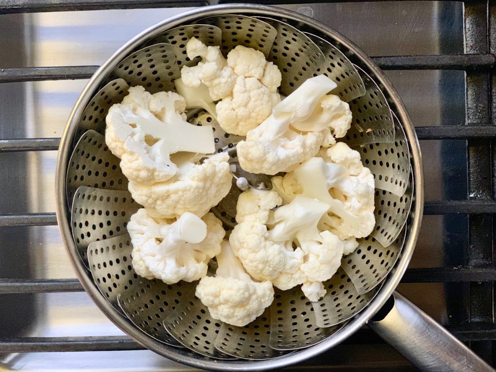 cauliflower in steamer basket in pot on stove