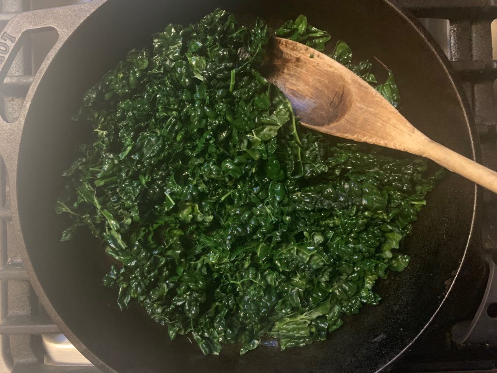 sautéed kale in cast iron skillet on stove with wooden spoon