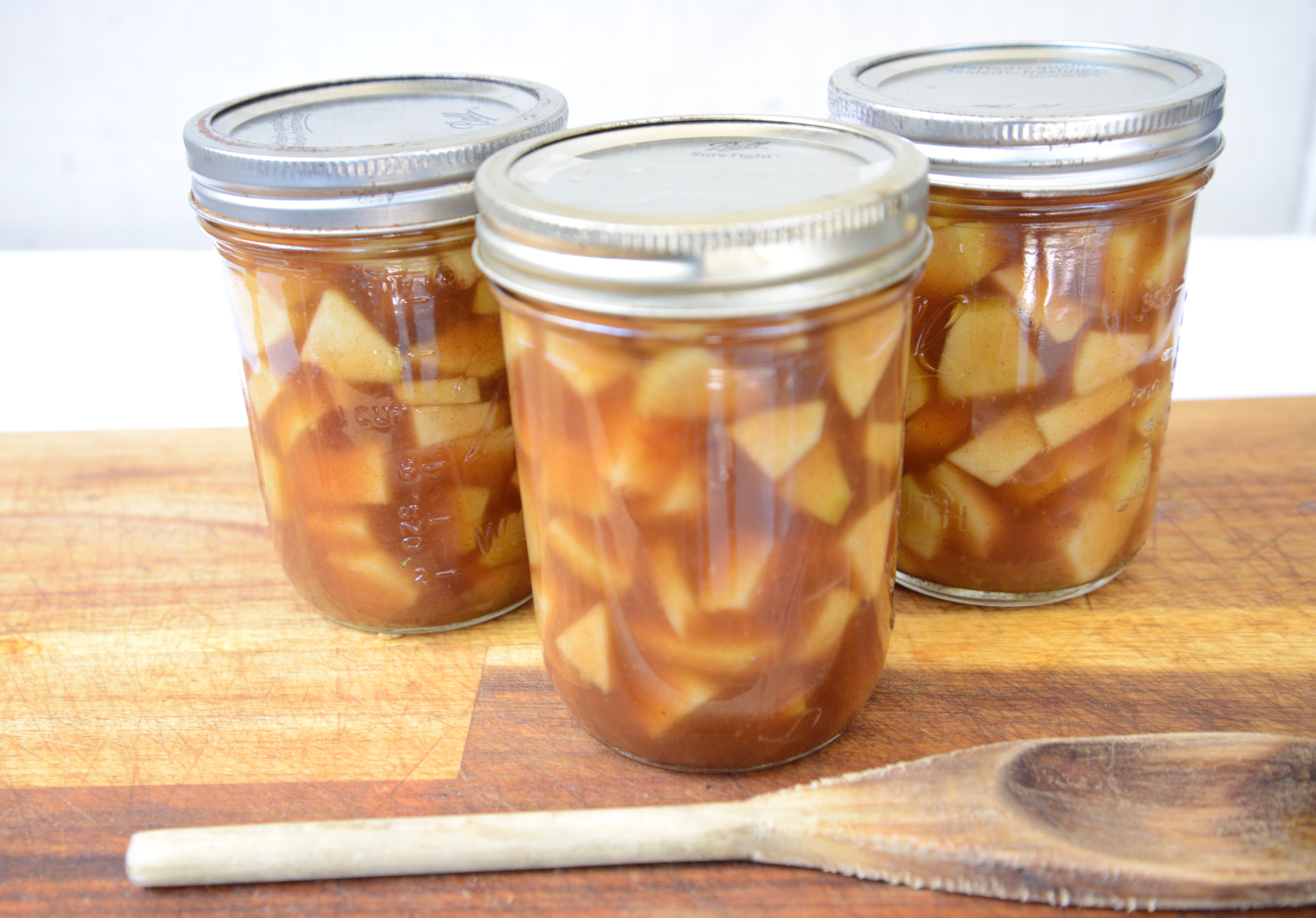 3 mason jars with canned apple pie filling on cutting board