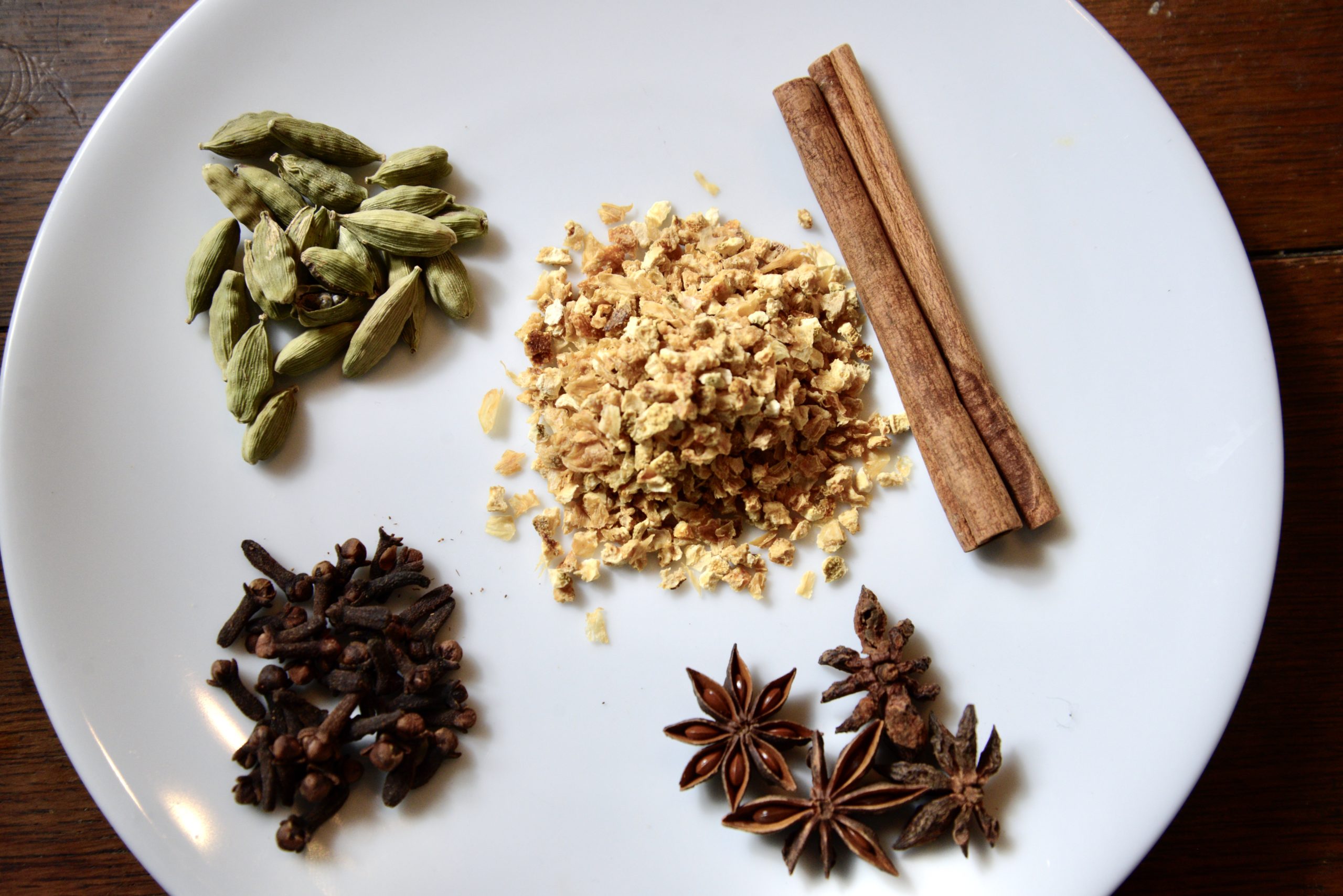 cinnamon stick, cardamon, cloves, star anise seed, and dried orange peels on a plate