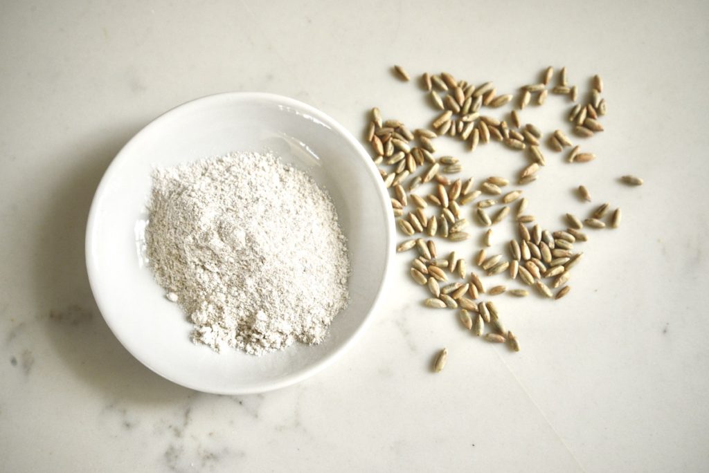 whole grain flour in a bowl and grain kernels