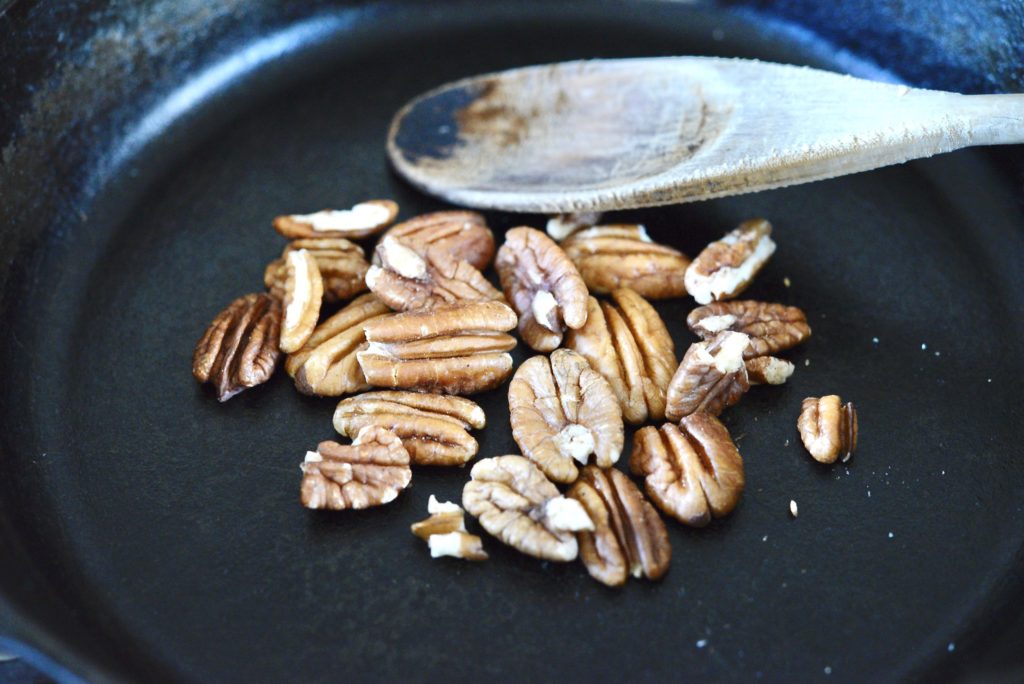 roasting pecans in cast iron skillet with wooden spoon