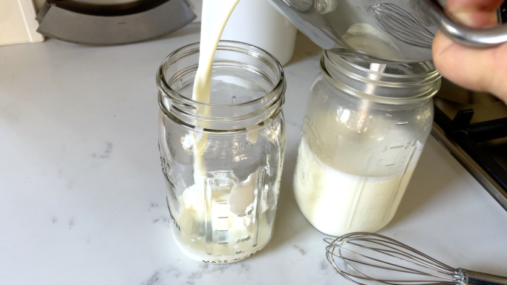 pouring warm milk into two quart size mason jars on kitchen counter