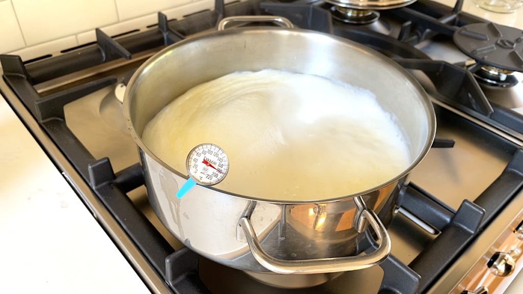 stainless steel pot on stove with yogurt and thermometer reading 180˚F